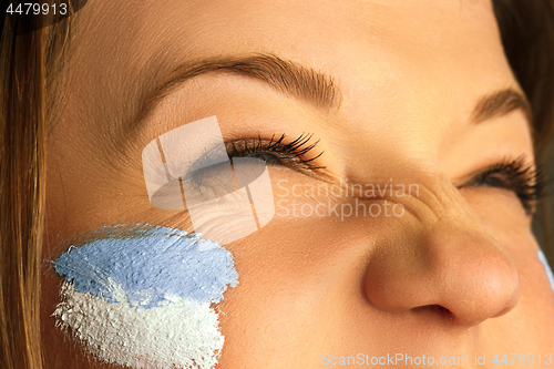 Image of Portrait of a woman with the flag of the Argentina painted on her face.