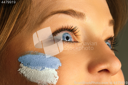 Image of Portrait of a woman with the flag of the Argentina painted on her face.