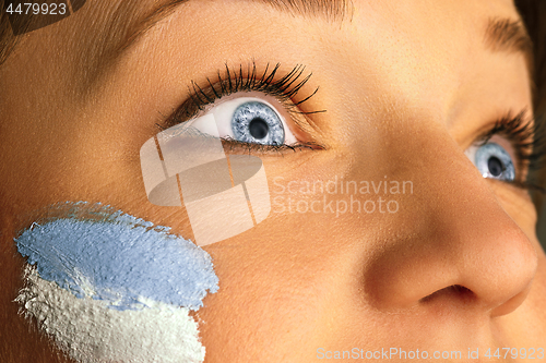 Image of Portrait of a woman with the flag of the Argentina painted on her face.