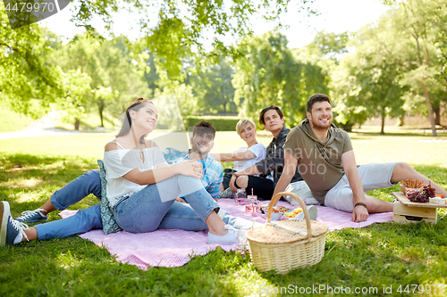 Image of happy friends with drinks at picnic in summer park