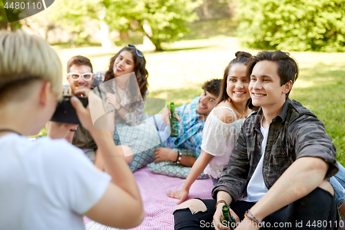 Image of friends with drinks photographing at summer picnic