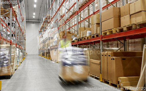 Image of worker carrying loader with goods at warehouse