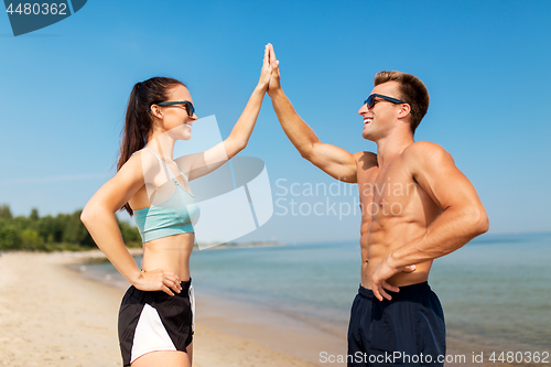 Image of happy couple in sports clothes and shades on beach