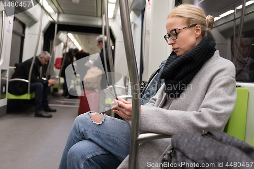 Image of Beautiful blonde woman wearing winter coat and scarf reading on the phone while traveling by metro public transport.