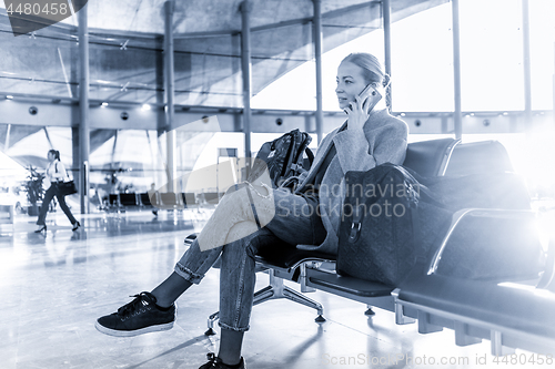 Image of Female traveler talking on her cell phone while waiting to board a plane at departure gates at airport terminal.