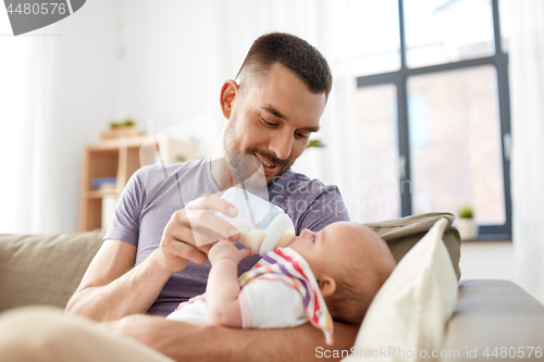 Image of father feeding baby daughter from bottle at home