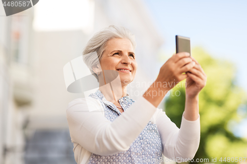 Image of senior woman photographing by smartphone in city