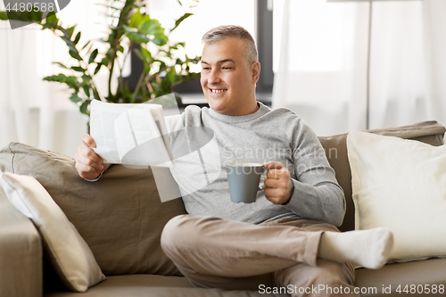 Image of man reading newspaper and drinking coffee at home