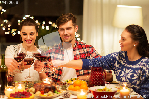 Image of happy friends drinking red wine at christmas party