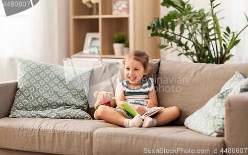 Image of happy girl sitting on sofa with book at home