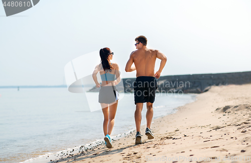 Image of couple in sports clothes running along on beach