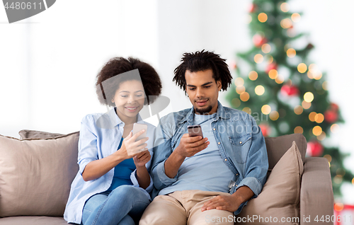 Image of happy couple with smartphones at home on christmas