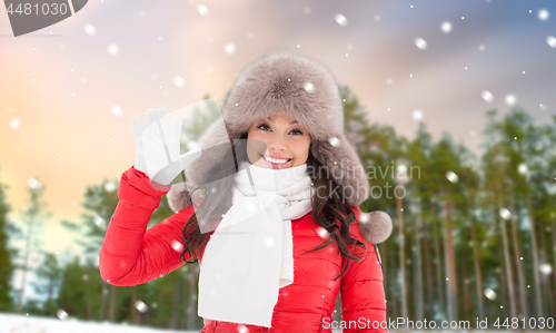 Image of happy woman in winter fur hat waving hand outdoors