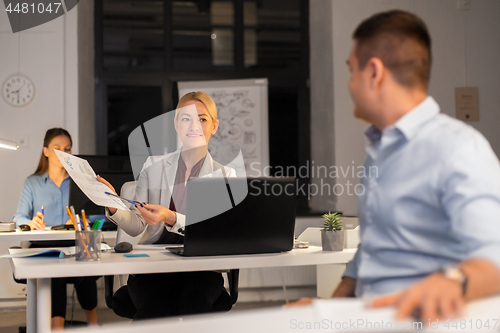 Image of woman showing charths to colleague at night office