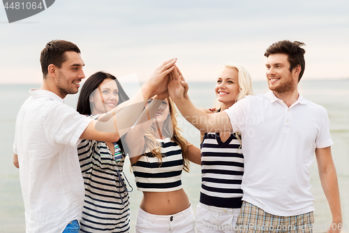 Image of happy friends making high five on beach