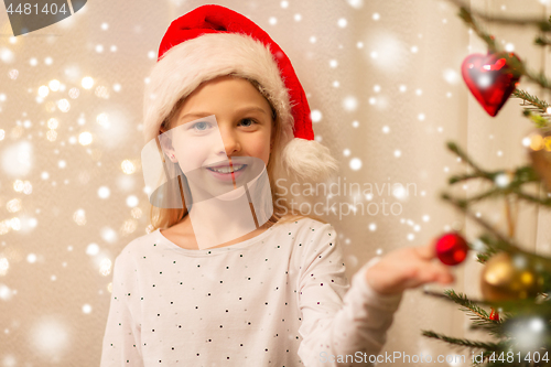 Image of happy girl in santa hat decorating christmas tree