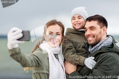 Image of family taking selfie by smartphone on autumn beach