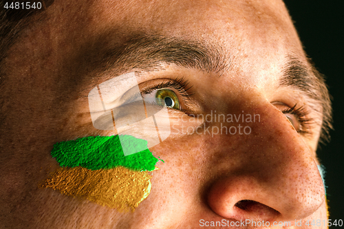 Image of Portrait of a man with the flag of the Brazil painted on him face.