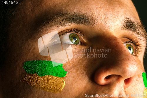 Image of Portrait of a man with the flag of the Brazil painted on him face.