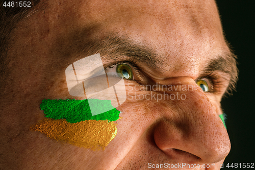 Image of Portrait of a man with the flag of the Brazil painted on him face.