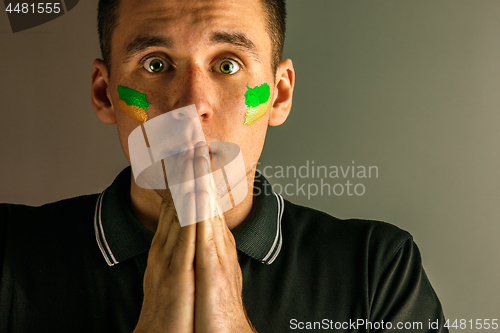 Image of Portrait of a man with the flag of the Brazil painted on him face.