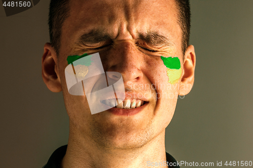 Image of Portrait of a man with the flag of the Brazil painted on him face.