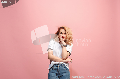 Image of The young woman whispering a secret behind her hand over pink background