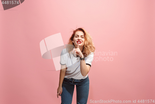 Image of The young woman whispering a secret behind her hand over pink background