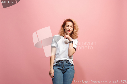 Image of The young woman whispering a secret behind her hand over pink background