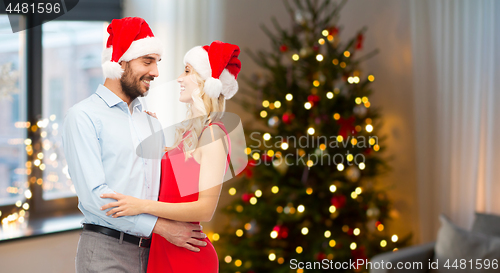 Image of happy couple in santa hats hugging on christmas