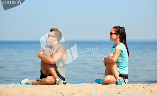 Image of smiling couple stretching legs on beach