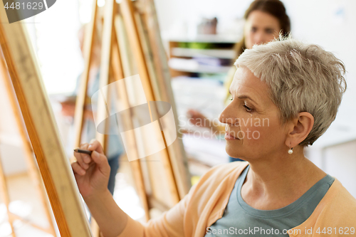 Image of senior woman drawing on easel at art school studio