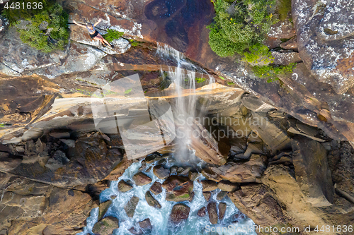 Image of Clifftop woman sitting by the edge of a waterfall tumbling into 