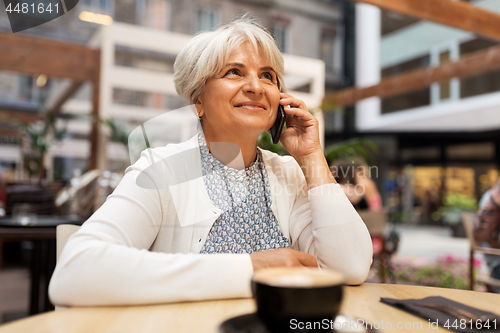 Image of senior woman calling on smartphone at street cafe