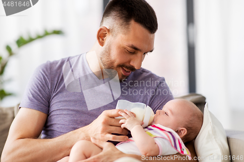 Image of father feeding baby daughter from bottle at home