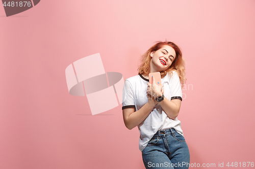 Image of The happy business woman is smiling and keeping in hand the smartphone against pink background.