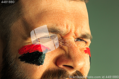 Image of Portrait of a man with the flag of the Germany painted on him face.