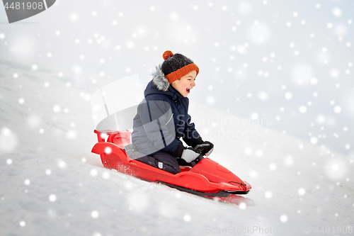 Image of happy boy sliding on sled down snow hill in winter