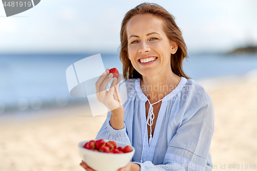 Image of happy woman eating strawberries on summer beach