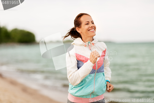 Image of smiling woman running along beach