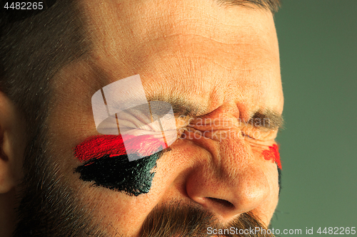 Image of Portrait of a man with the flag of the Germany painted on him face.