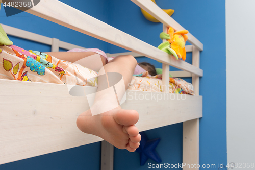 Image of The child sleeps on the second floor of a bunk bed, the leg hangs down