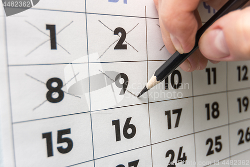 Image of Pencil crosses out dates on the wall calendar