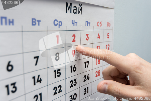 Image of Hand points to the May 2 holiday on a wall calendar sheet