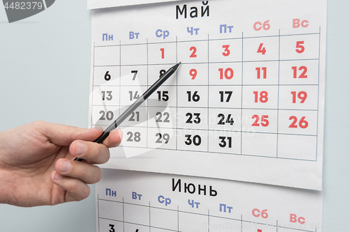 Image of Pencil hand indicates long weekends and holidays on a wall calendar