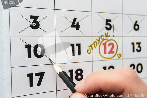 Image of A hand crosses out the penultimate day before the holiday with a pencil in the calendar