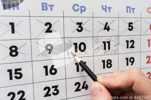 Image of Hand cross out the last working day with a pencil in the calendar before the holiday