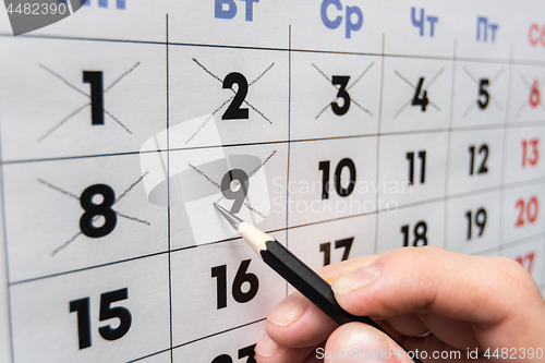 Image of Pencil crosses out dates on the wall calendar