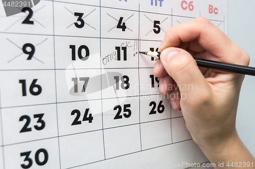 Image of The hand with a pencil writes the word vacation in the wall calendar