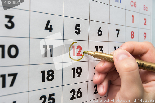 Image of Hand with a marker on the wall calendar leads around a red holiday